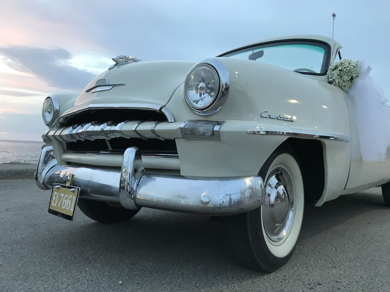 Η ιβουάρ Plymouth cabriolet του 1953 στολισμένη για γάμο, δίπλα στη θάλασσα στο ηλιοβασίλεμα